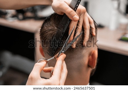 Barber uses scissors and a comb to cut the hair on the back of a man's head in a barbershop.