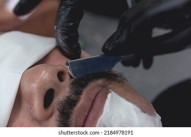 A Barber Uses A Straight Edge Razor To Thin And Shape The Upper Part Of A Client's Mustache.