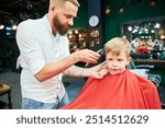 Barber using comb and shaver to cut hair. Professional hairdresser shaving little kid