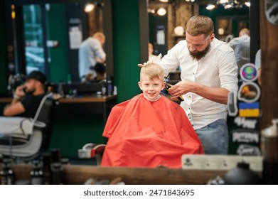 Barber using comb and shaver to cut hair. Professional hairdresser shaving little kid's nape. - Powered by Shutterstock