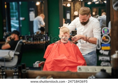 Barber using comb and shaver to cut hair. Professional hairdresser shaving little kid's nape.