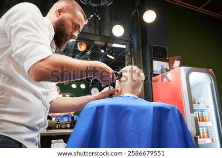 Barber using comb and shaver to cut hair. Professional hairdresser shaving little kid's nape.
