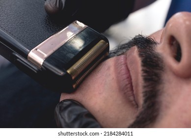 A Barber Using An Electric Foil Shaver To Get A Close Shave Of The Chin Area. Closeup Shot Of Procedure At A Barbershop.