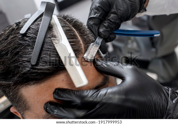 A\
barber wearing gloves uses a shaving knife to create a hard part.\
Classic and trendy haircut style. At a\
barbershop.