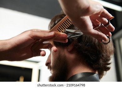 Barbershop. Brunet man getting haircut by a hairdresser while sitting in a chair at barbershop. 