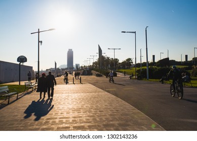 Barcelona, Spain - 05.12.2018: Beautiful Sunny Day With People Cycling And Walking Along A Street Close To The Beach