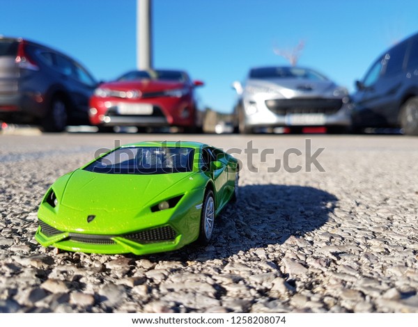Barcelona / Spain 10 12 2018: Green toy car\
stands in the parking lot on the background of real cars. Parking\
problems in the city and paid parking\
space