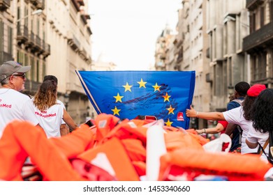 Barcelona, Spain- 17 July 2019: Open Arms Activists March Holding Rubber Dinghy Boat With Lifebelts As A Symbol Of Mediterranean Sea Migrants Deaths With European Union Flag