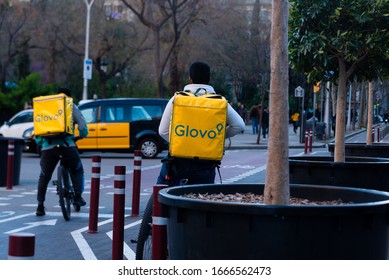 Barcelona, Spain - 20 February 2020: Young Riders Working For Glovo Delivery Service Riding Bike In The City In The Evening. Food Delivery Plays A Mayor Role In The New Gig Economy