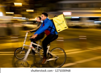 Barcelona, Spain - 21 December 2018: Young Riders Working For Glovo Delivery Service Riding Bike In The City At Night. Food Delivery Plays A Mayor Role In The New Gig Economy.