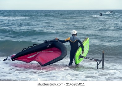 Barcelona, Spain - April 8, 2022: Man with wing foil equipment of colorful colors, entering the sea, fashionable sport on the beaches, a hobby that mixes adrenaline and ecology.