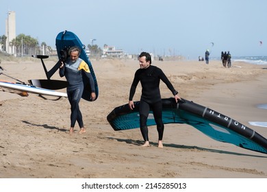 Barcelona, Spain - April 8, 2022: Two friends with wing foil fans talk on the sand of the beach, a trendy water sport, a hobby that mixes adrenaline and ecology.