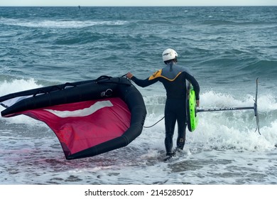 Barcelona, Spain - April 8, 2022: Man with wing foil equipment of colorful colors, entering the sea, fashionable sport on the beaches, a hobby that mixes adrenaline and ecology.
