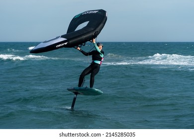 Barcelona, Spain - April 8, 2022: Middle-aged woman practicing wing foil with dexterity, approaching the shore at high speed, fashionable sport on the beaches, hobby that mixes adrenaline and ecology