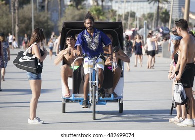 BARCELONA, SPAIN - JULY 31, 2016: Young rickshaw gives a lift to cheerful tourists along the beach in Barcelona, Spain