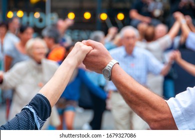 Barcelona, España. Vista de personas mayores tomándose de la mano y bailando la danza nacional Sardana en Plaza Nova, Barcelona, España. Manos viejas frente a gente borrosa