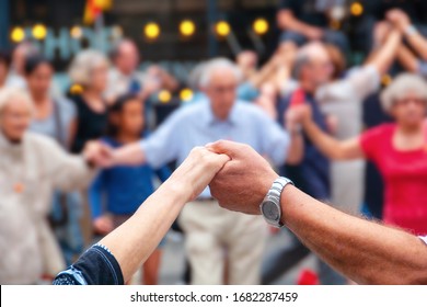  Barcelona, Spanien. Aussicht auf Senioren, die Händchen halten und nationalen Tanz Sardana auf der Plaza Nova, Barcelona, Spanien tanzen. Alte Hände vor unscharfen Menschen