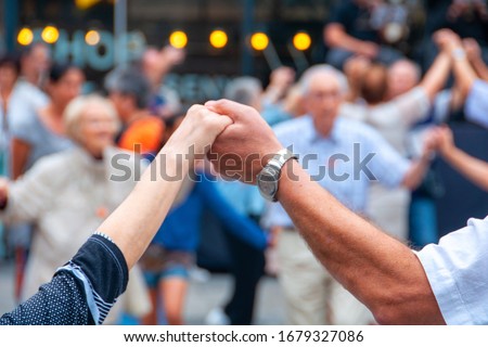 Barcelona, Spain. View of senior people holding hands and dancing national dance Sardana at Plaza Nova, Barcelona, Spain. Old hands in front of blurred people