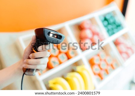 Barcode scanner in woman's hand on fruit shelf background, supermarket spending concept