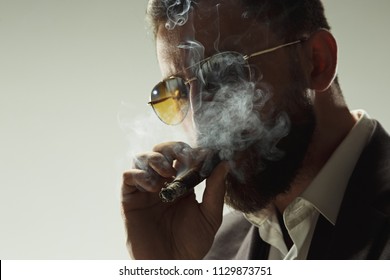 The Barded Man In A Suit Holding Cigar. Stylish Business Man On Gray Studio Background. Beautiful Male Portrait. Young Emotional Man. The Human Emotions, Facial Expression Concept. Italian Look