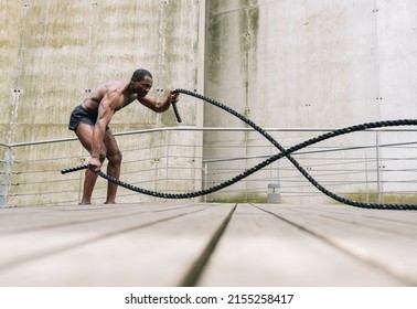 Bare Chested African American Man Exercising With Battle Ropes In Gym. Elite Athlete Concept