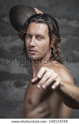 bare chested long hair model is  throwing football ball in camera