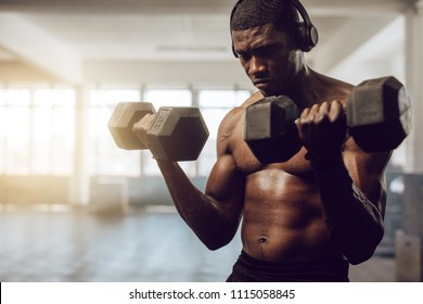 Bare Chested Man Listening To Music During Workout At The Gym. Athletic Man Lifting Dumbbells Wearing Wireless Headphones.