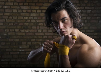 Bare chested young Malaysian boxer wrapping straps around hands