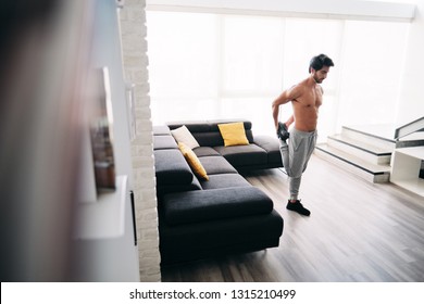 Bare Chested Young Man Stretching Muscles Before Starting A Workout Routine. Handsome Hispanic Male Athlete Exercising For Wellness In His Living Room. Latino People Doing Fitness And Sport At Home.