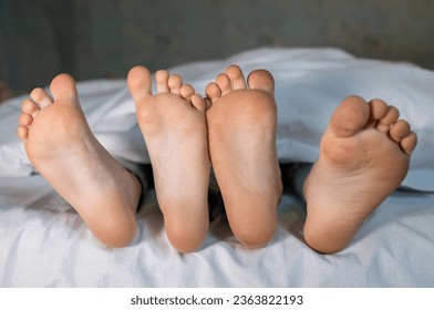 the bare, clean feet of two children, offspring, lying side by side under the same blanket on the bed. morning relaxation, cozy rest. cute pictures of baby feet - Powered by Shutterstock