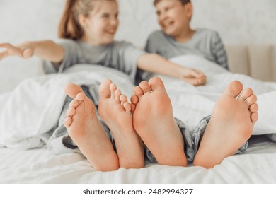 the bare, clean feet of two children, offspring, lying side by side under the same blanket on the bed. morning relaxation, cozy rest. cute pictures of baby feet - Powered by Shutterstock