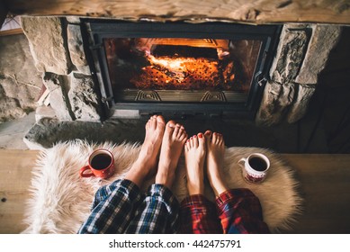 Bare couple feet by the cozy fireplace. Man and Woman relaxes by warm fire with a cup of hot drink and warming up her feet. Close up on feet. Winter and Christmas holidays concept - Powered by Shutterstock