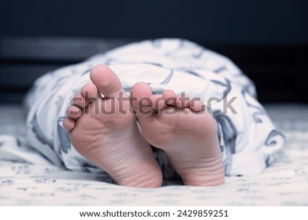 Bare feet of a child. The child's legs look out from under the blanket. Foot and leg