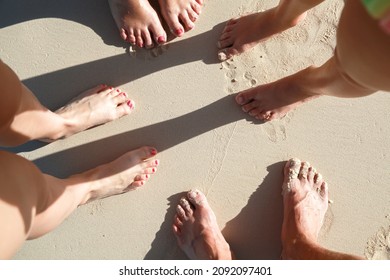 Bare Feet Of A Family Members Standing On Wet Coastal Sand On A Sunny Day, Top View