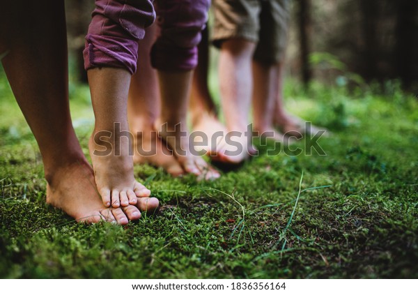 Bare feet of family with small\
children standing barefoot outdoors in nature, grounding\
concept.