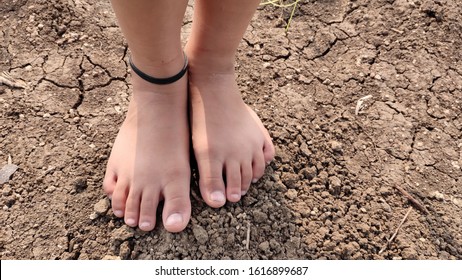 Bare Feet Of A Little Girl Wearing Black Thread As Anklet Standing On Soil.