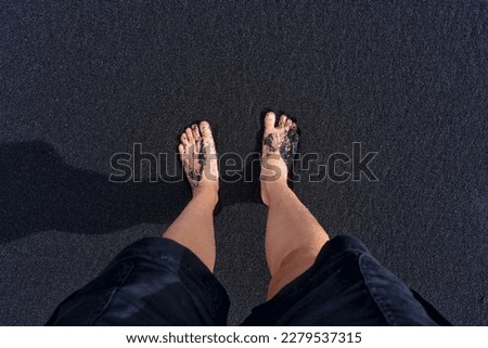 Bare feet on black oceanic sand, top view. Organic background related to travel, nature and relaxation.