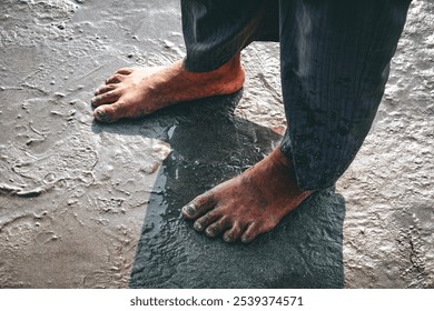 Bare feet on wet sandy ground with rippled water patterns beside dark pants. - Powered by Shutterstock