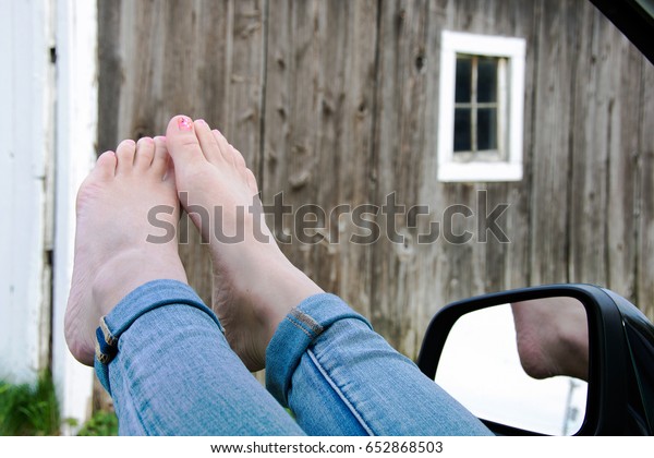 bare feet\
out of car window with old barn\
background