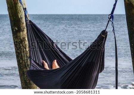 Bare feet of a young white man in a hammock slung between wooden piles of a fishing pier along the Atlantic coast of South Carolina, USA, on a sunny afternoon. Foreground focus.