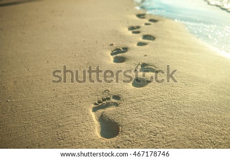 bare footsteps on the sand on a beach. the sand is white and the steps can be of man or women. Footsteps on the coral sandy beach