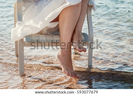 Bare legs girl in a white dress touched the sea water..