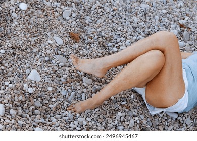 Bare legs resting on a pink blanket placed on a pebbled beach, creating a relaxed and tranquil scene. - Powered by Shutterstock