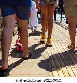 Bare Legs Walking On The Road With A Small Child In A White Panama Hat In Summer