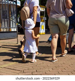 Bare Legs Walking On The Road With A Small Child In A White Panama Hat In Summer