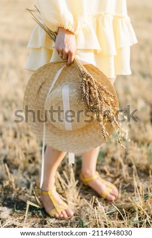 Bare legs of a young girl on a summer day. girl in a yellow dress. Large straw hat with a bouquet of wheat. Agricultural texture