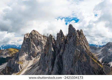 Bare peak and steep slopes of Seceda mountain range against cloudy sky. Observation deck overlooking giant ridgeline in Alps aerial view