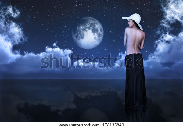 bare\
woman looking at full moon between clouds over\
water