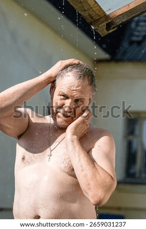 A bare-chested man cools off in the heat under a stream of summer rain flowing down from a roof