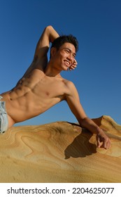 Bare-chested Young Man Lie On A Large Stone On The Beach.